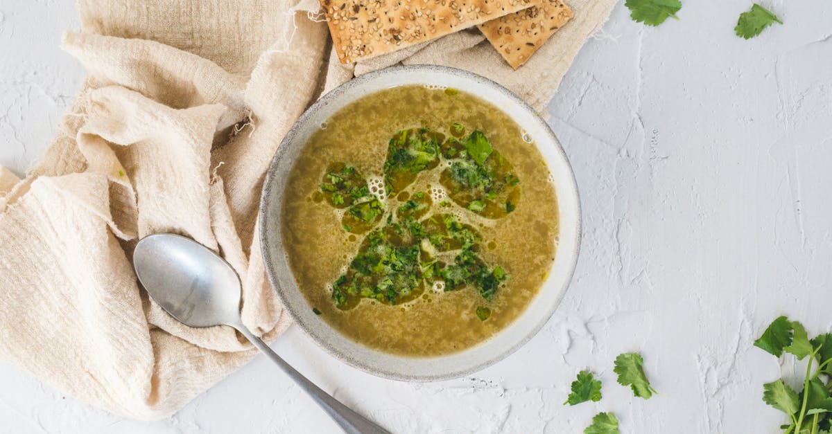 a bowl of fresh herb soup served with crackers and a spoon on a light background