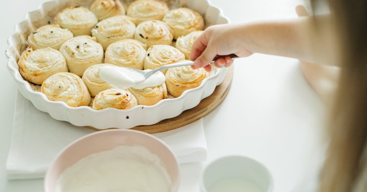 a child spreads creamy icing over freshly baked cinnamon rolls highlighting a cozy food preparation