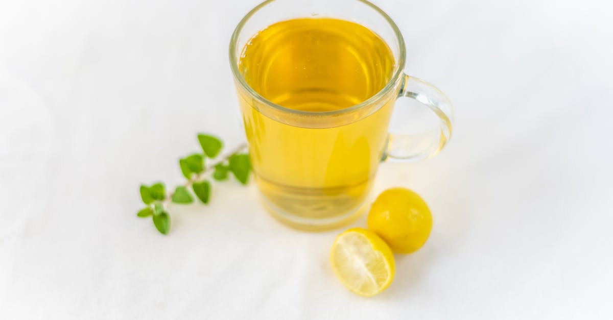 a clear glass of lemon herbal tea accompanied by fresh herbs on a white surface offering a refreshi