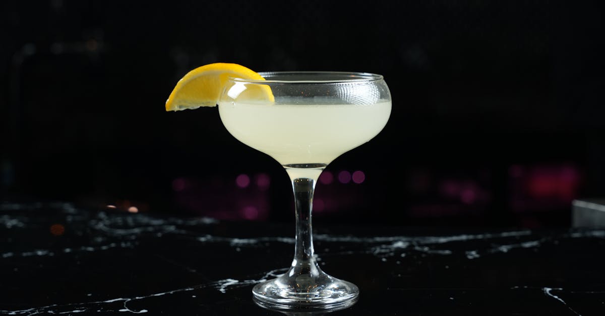 a close up of a cocktail with a lemon slice on a black marble countertop ideal for bar themes
