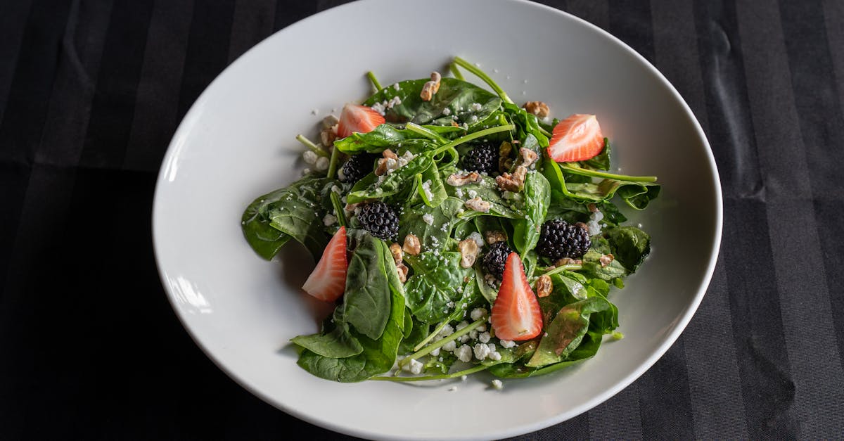 a close up of a fresh spinach salad with strawberries walnuts and blackberries on a white plate