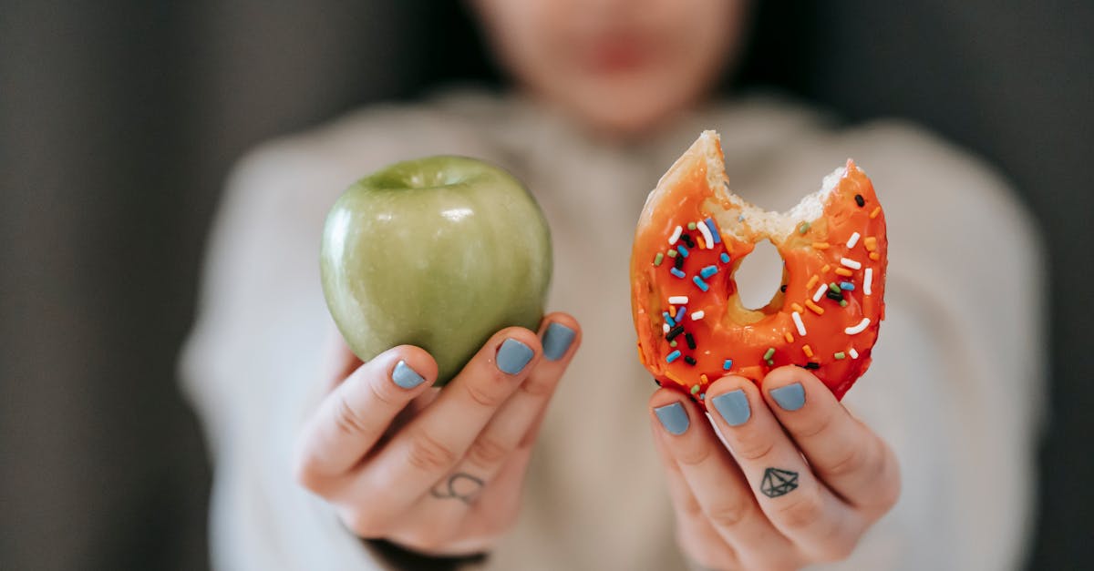 a close up of a person holding an apple and a donut symbolizing the choice between healthy eating a