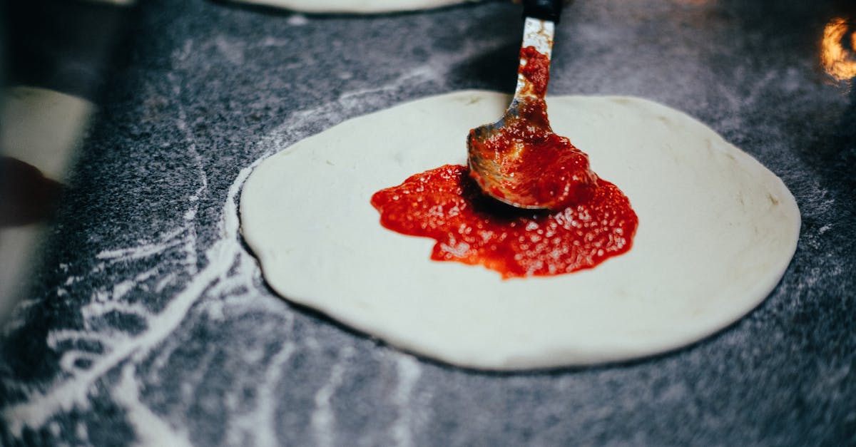 a close up of a spoon spreading tomato sauce on pizza dough capturing the pizza making process