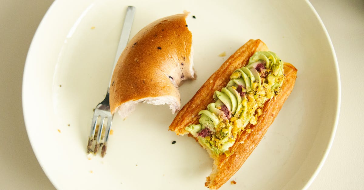 a close up of a tasty avocado tartine with a half bagel on a simple white plate