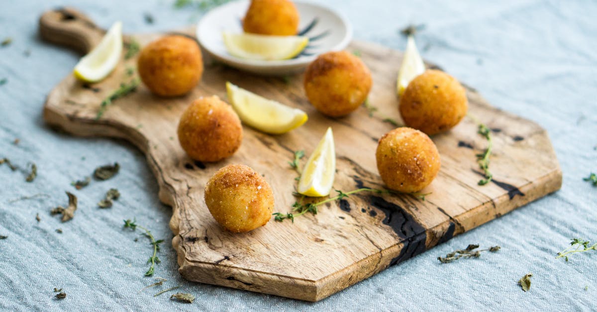 a close up of crispy homemade arancini served with lemon slices on a rustic wooden board 5