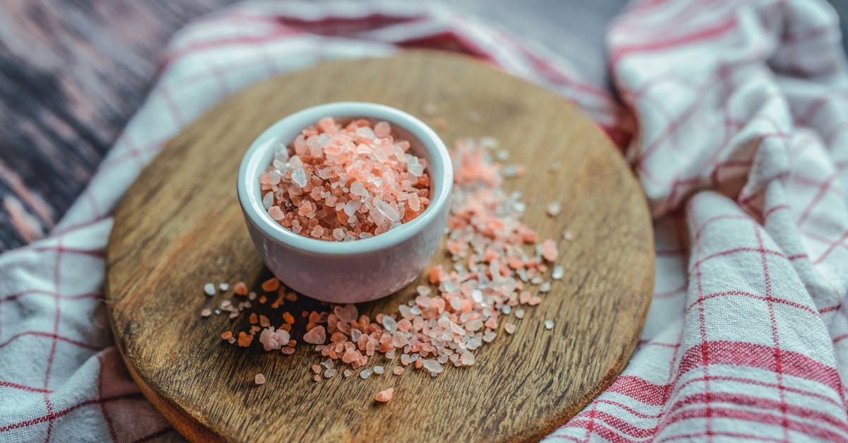 a close up shot of pink himalayan salt in a ceramic cup on a wooden board ideal for culinary and he