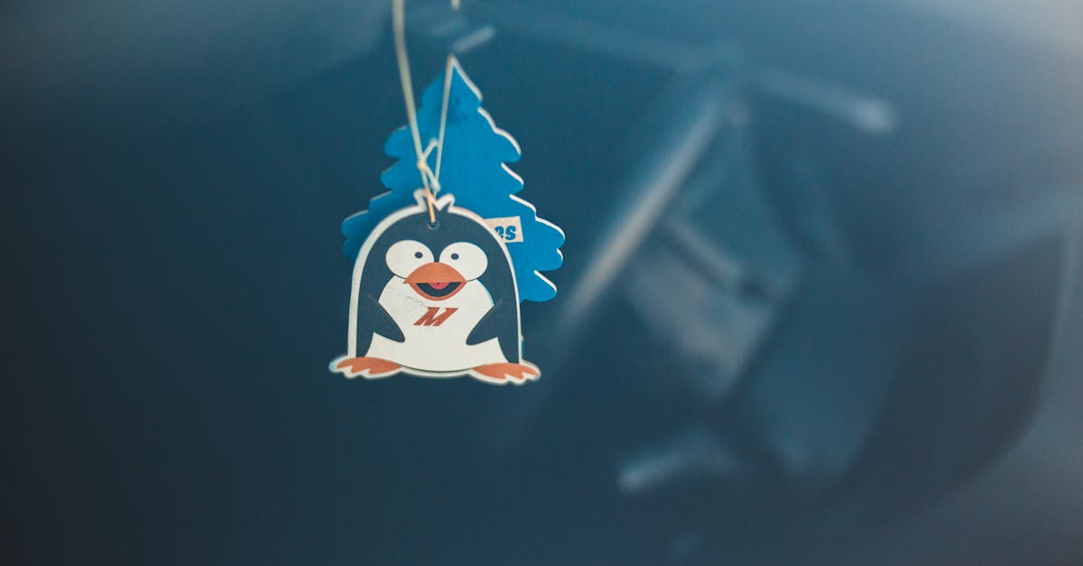 a cute penguin themed air freshener hanging in a car with soft focus background