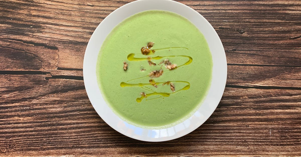 a delicious creamy broccoli soup garnished with walnuts and olive oil served in a white bowl on a r 4
