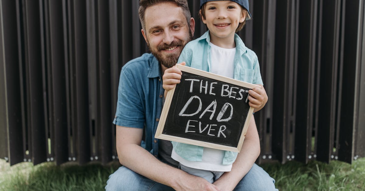 a father and son smiling together holding a best dad ever sign outside