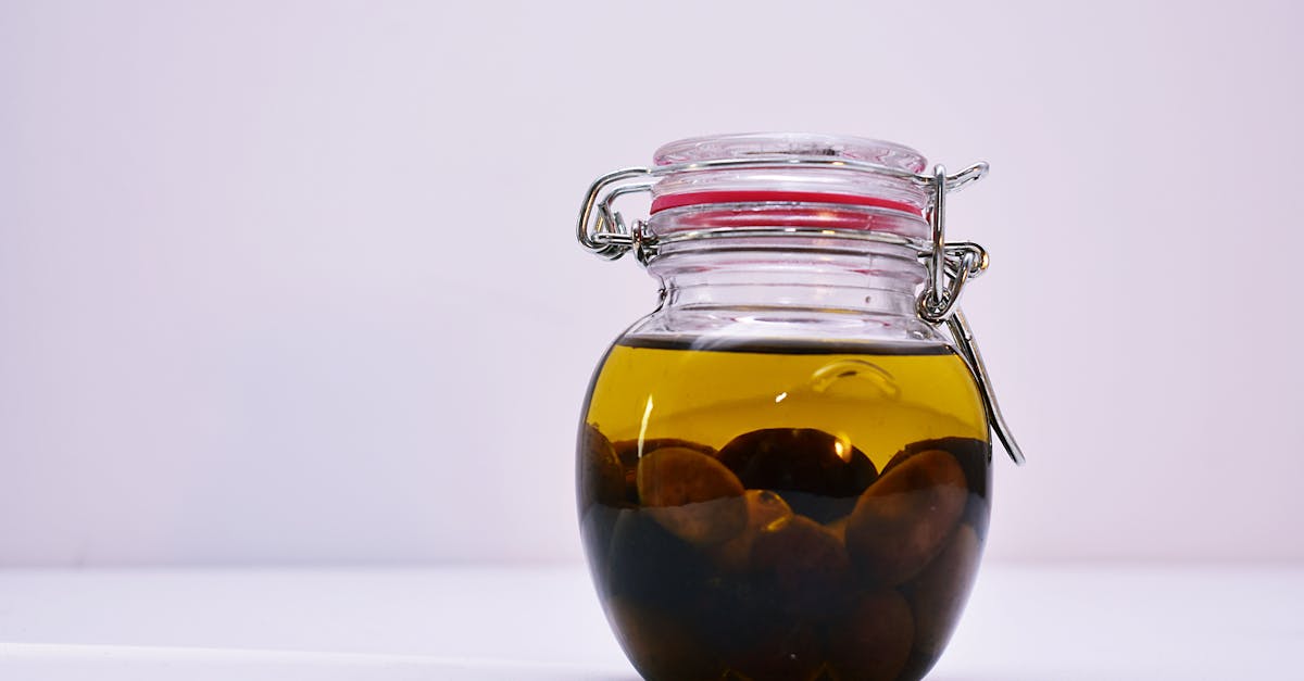 a glass jar containing olives submerged in oil with a sealed lid on a white background 2