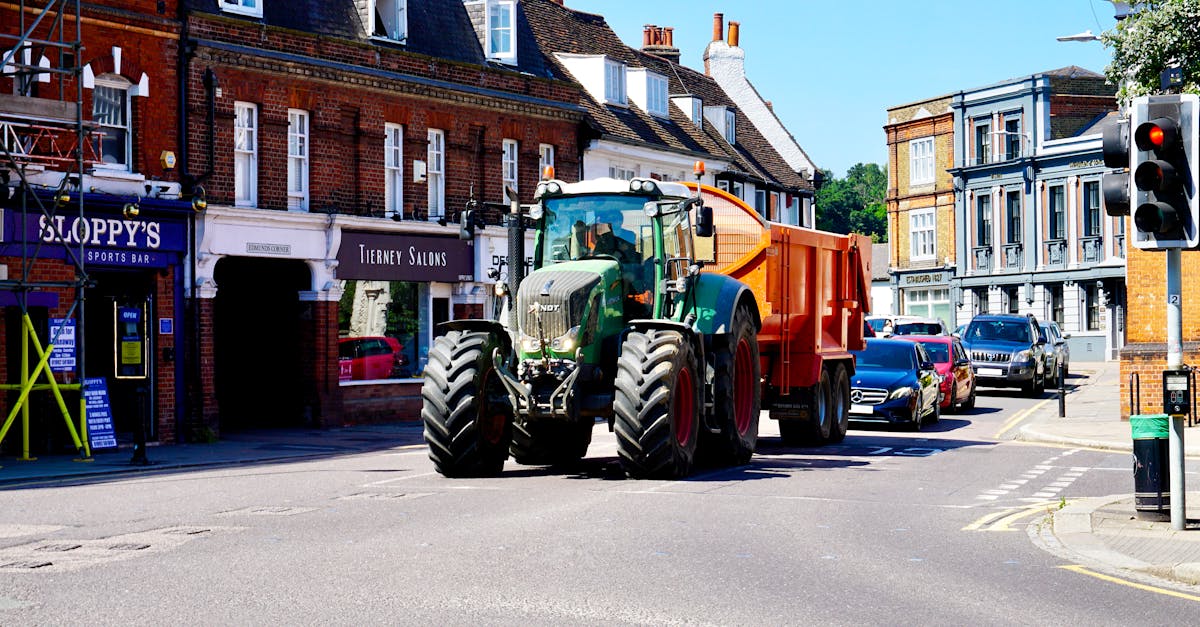 a green tractor drives through hertford town center surrounded by cars and shops