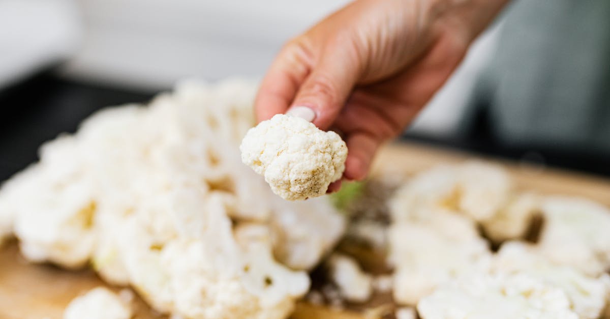 a hand holds a fresh cauliflower floret over a wooden board with scattered florets showcasing a coo
