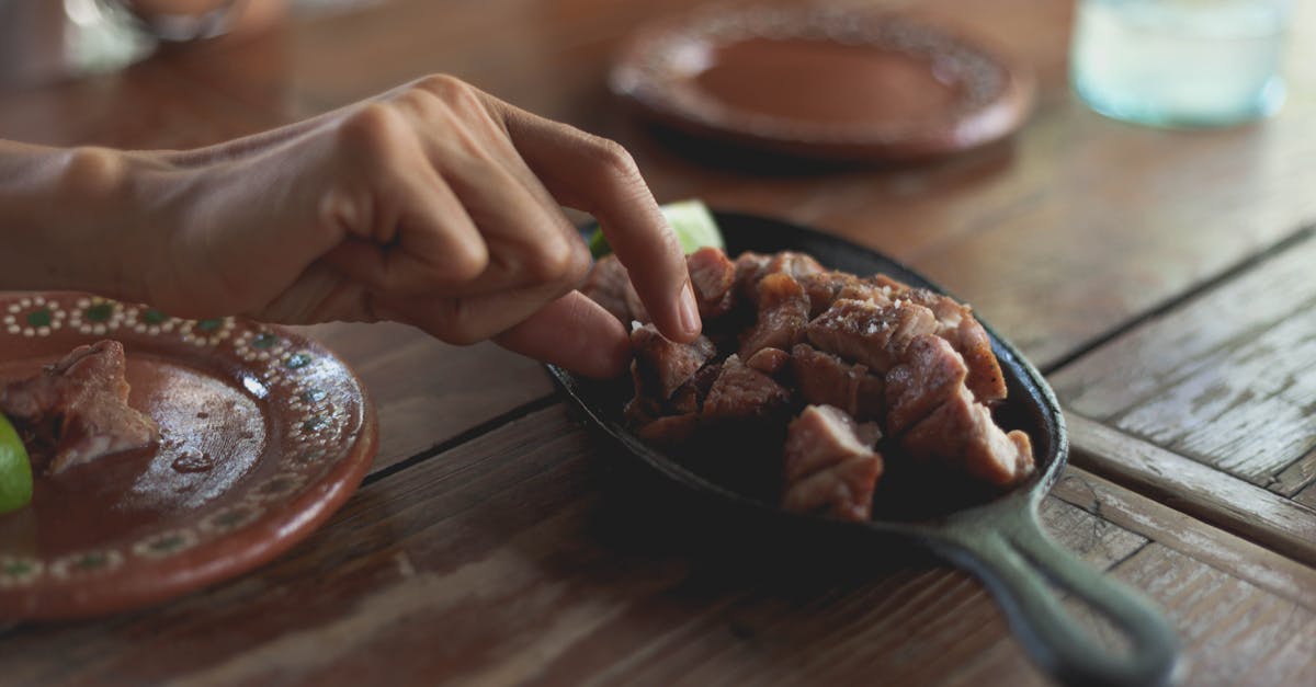a hand picking grilled steak pieces on a cast iron pan over a rustic wooden table