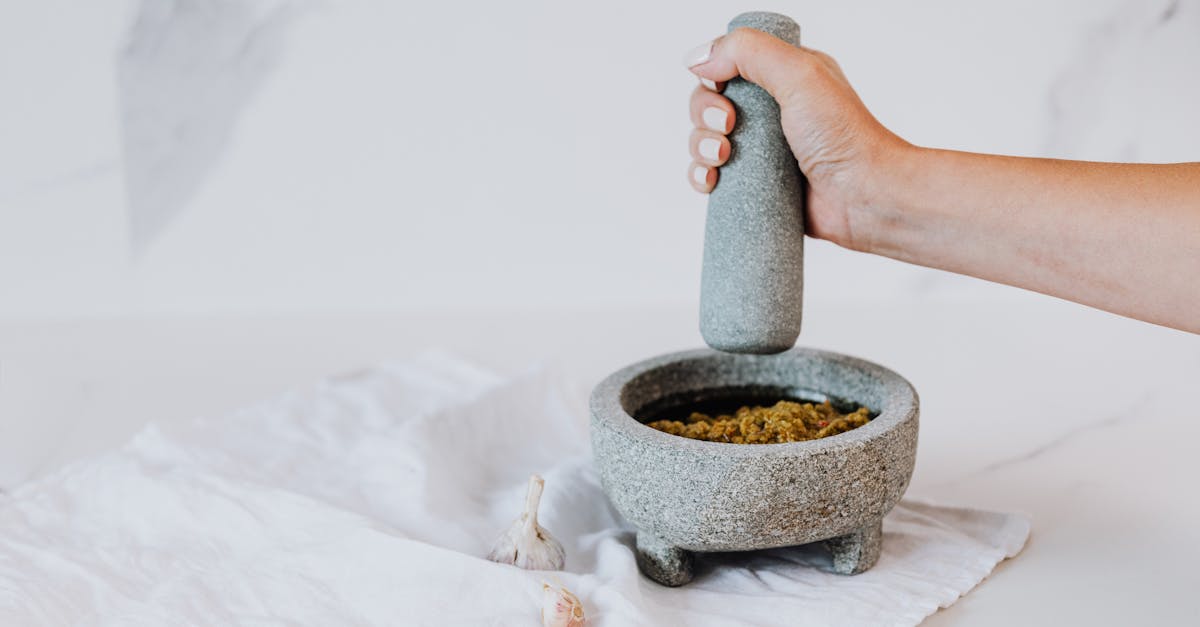 a hand using a stone mortar and pestle to make pesto with fresh ingredients 1