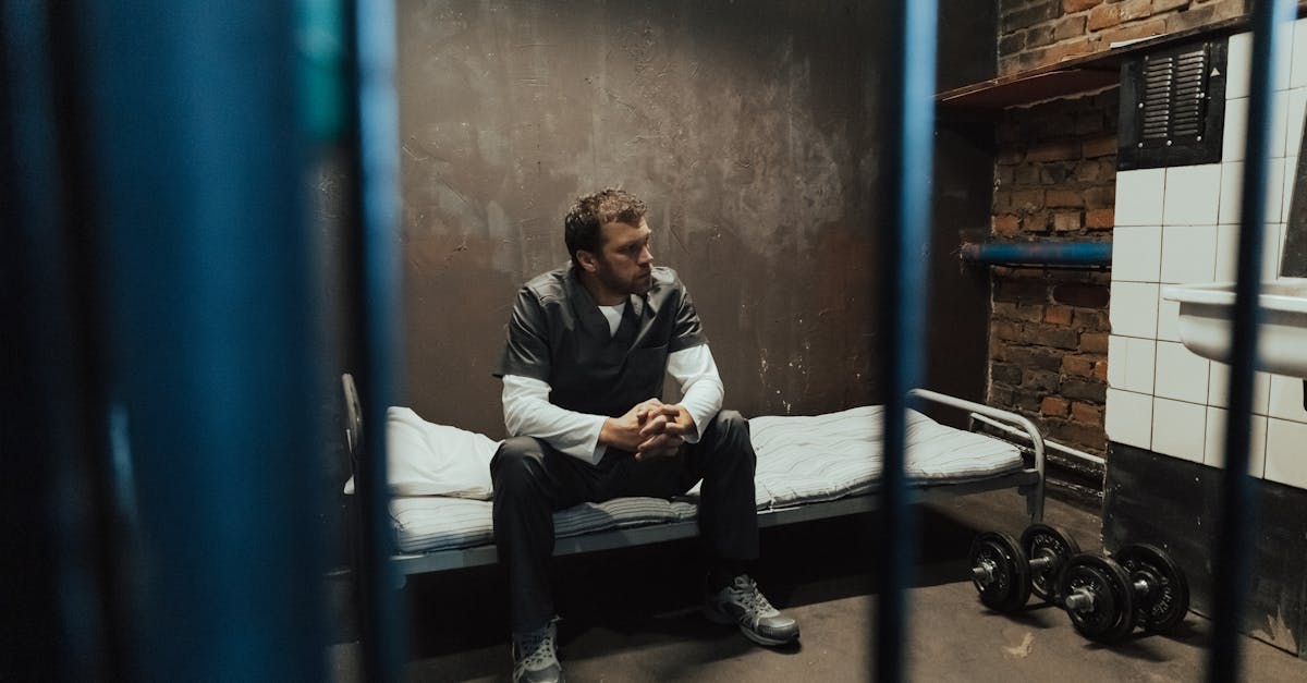 a man in prison uniform sitting on a bed in a dimly lit jail cell