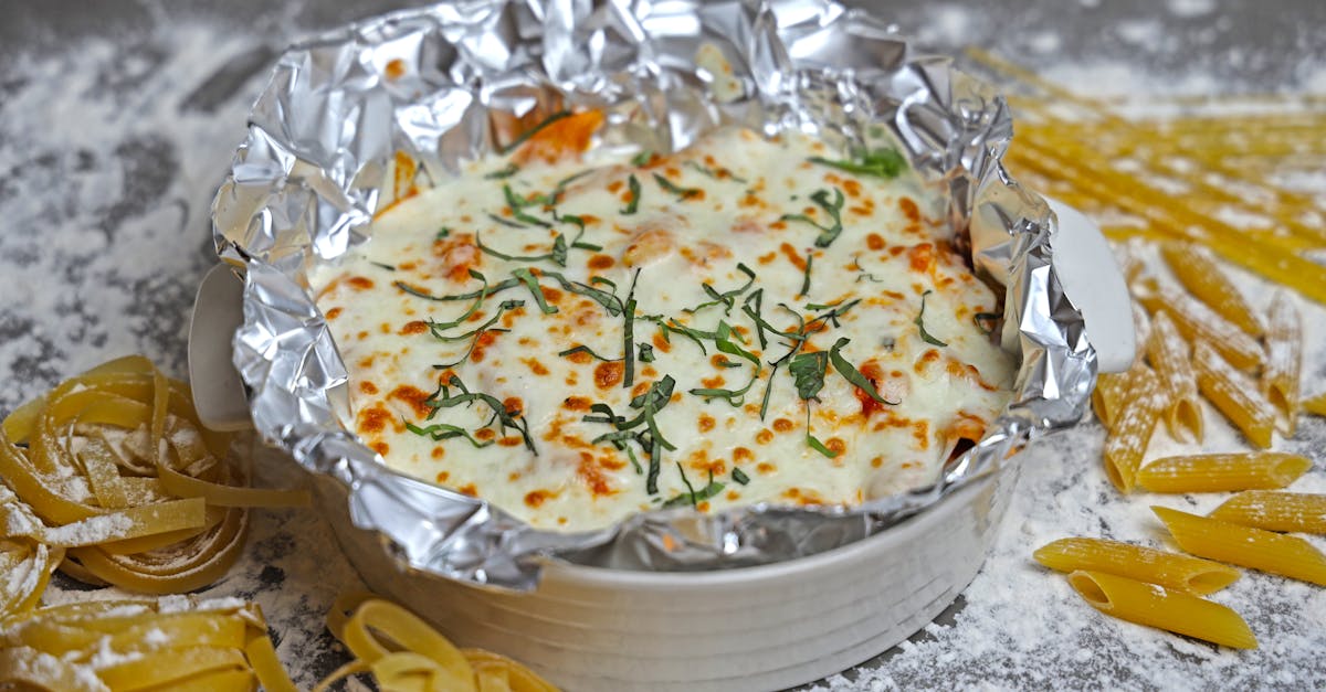 a mouthwatering image of baked pasta topped with cheese and fresh herbs surrounded by raw pasta and
