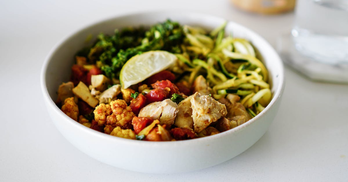 a nutritious bowl containing zoodles roasted cauliflower chicken and a lemon slice perfect for h