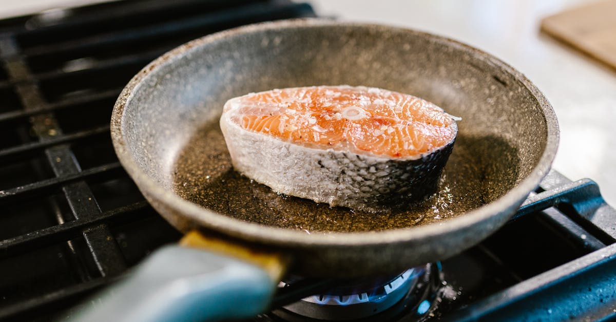 a salmon steak is searing in an iron frying pan on a stove showcasing cooking detail