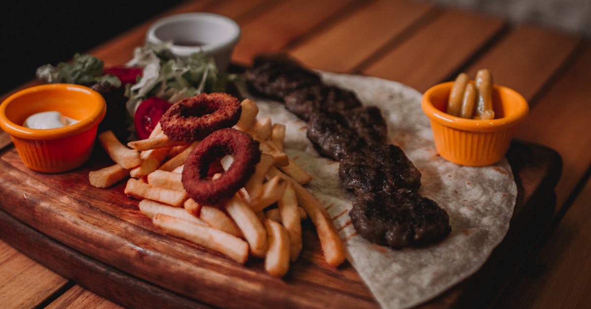 a tasty fast food tray featuring onion rings fries and seasoned meat on a cutting board