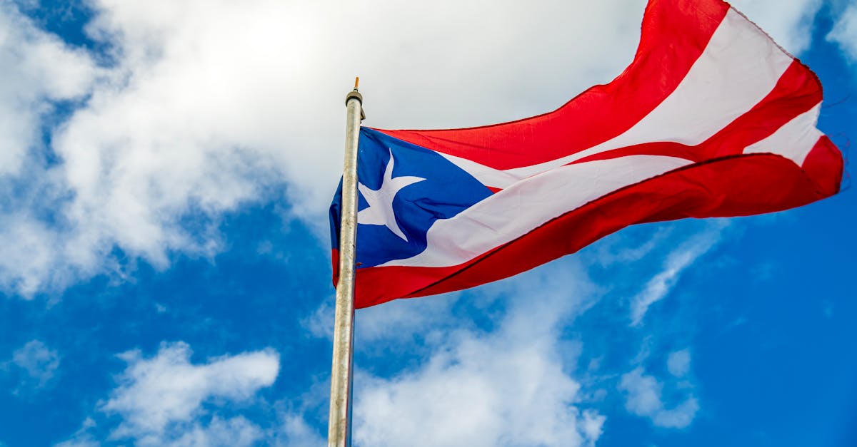 Home a vibrant puerto rican flag waving on a flagpole against a bright blue sky with clouds 1