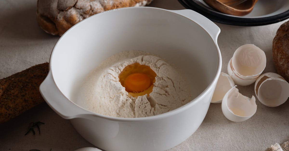a white bowl with flour and egg surrounded by bread and utensils on a kitchen counter