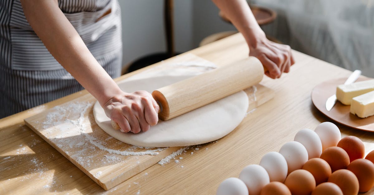 a woman rolls out dough on a floured surface with eggs and butter nearby