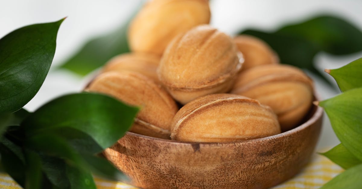 a wooden bowl filled with tasty walnut shaped cookies surrounded by green leaves and soft light