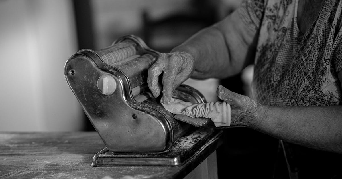 an elderly woman uses a pasta machine to prepare homemade pasta captured in black and white