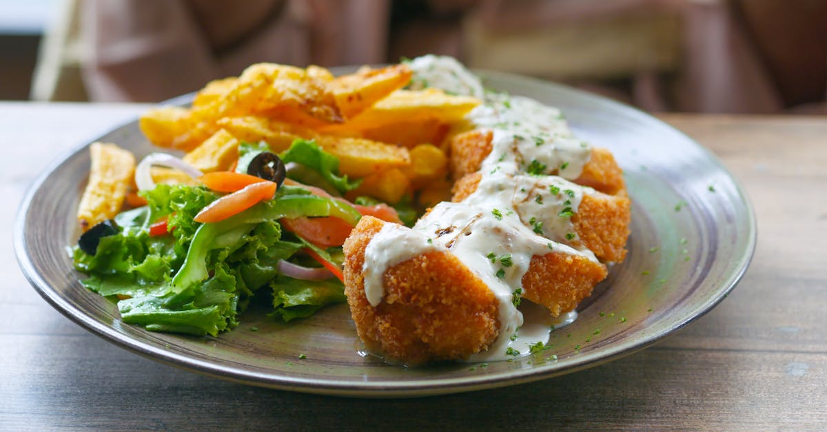 appetizing close up of breaded chicken with creamy sauce fries and fresh salad