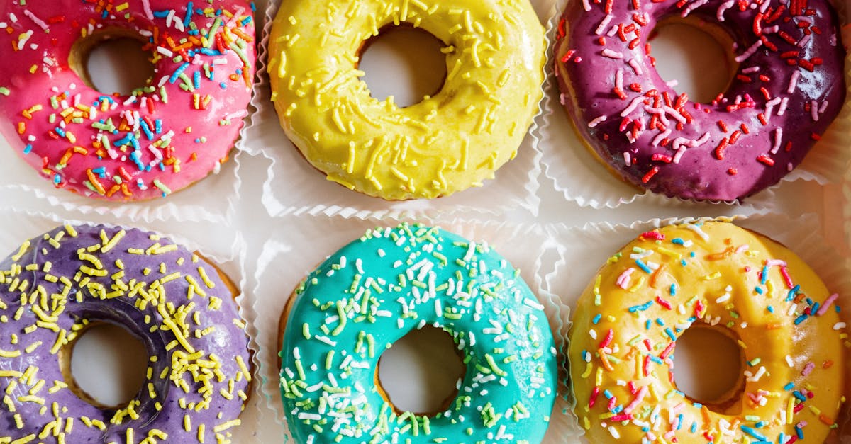 assorted colorful glazed donuts with sprinkles arranged in a flat lay