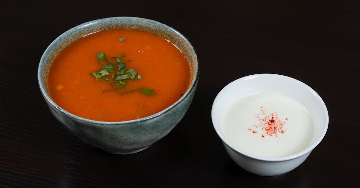 bowl of tomato soup garnished with herbs served alongside a creamy dip on a dark surface 1