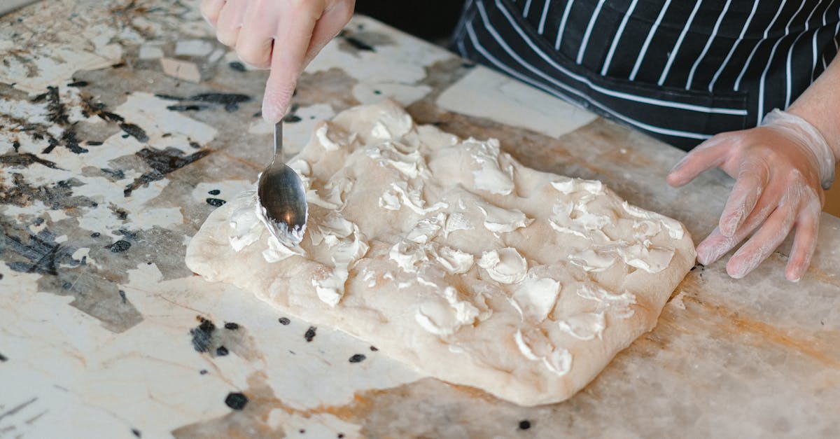 chef in apron spreading cheese on dough using spoon at marble work table 2