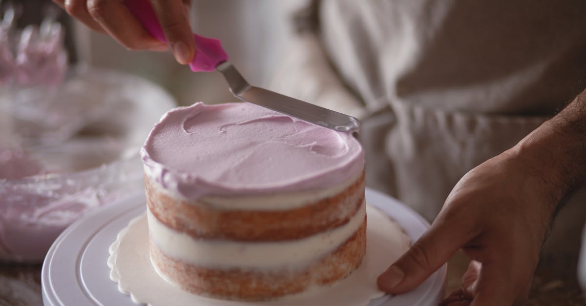 close up of a baker skillfully frosting a naked cake with pastel icing