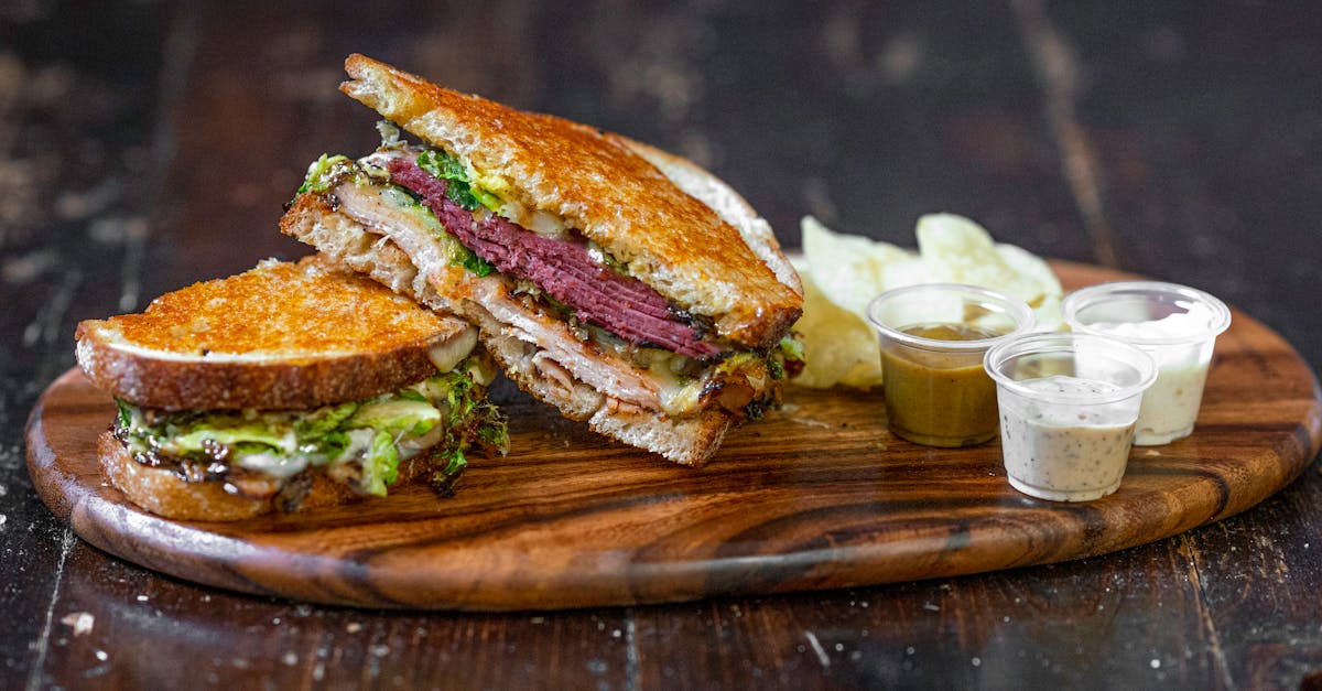close up of a gourmet sandwich with various dips on a wooden tray