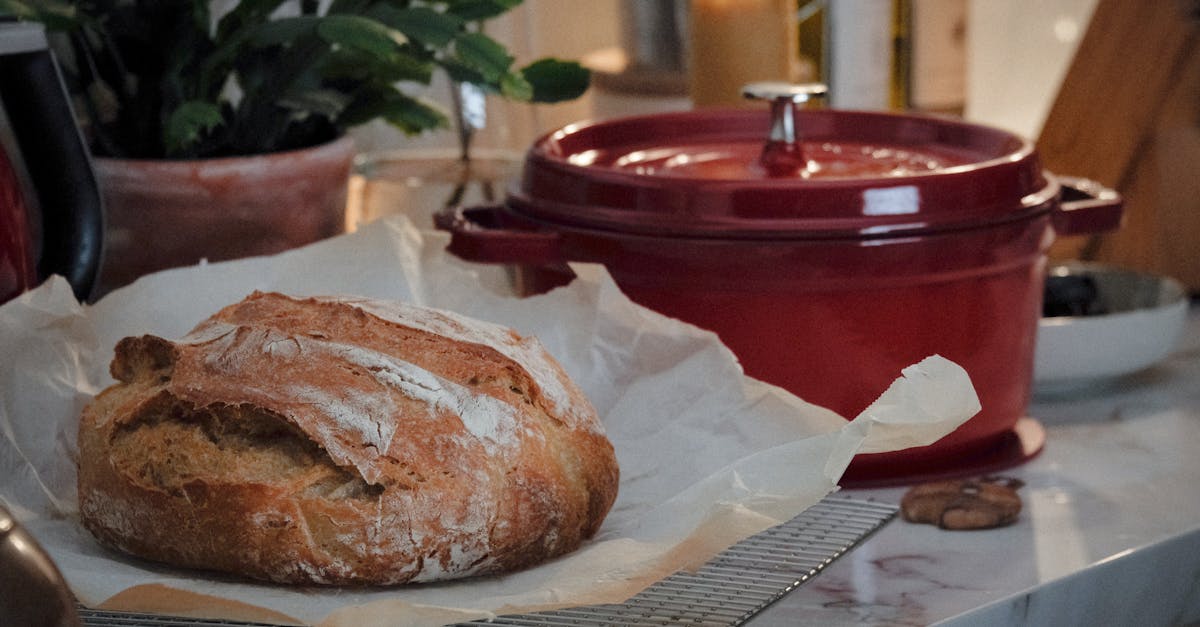 close up of a rustic loaf of bread on a kitchen counter with a red dutch oven nearby