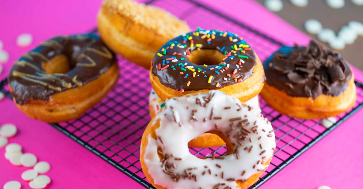 close up of assorted glazed donuts with sprinkles on a rack over a vibrant pink backdrop