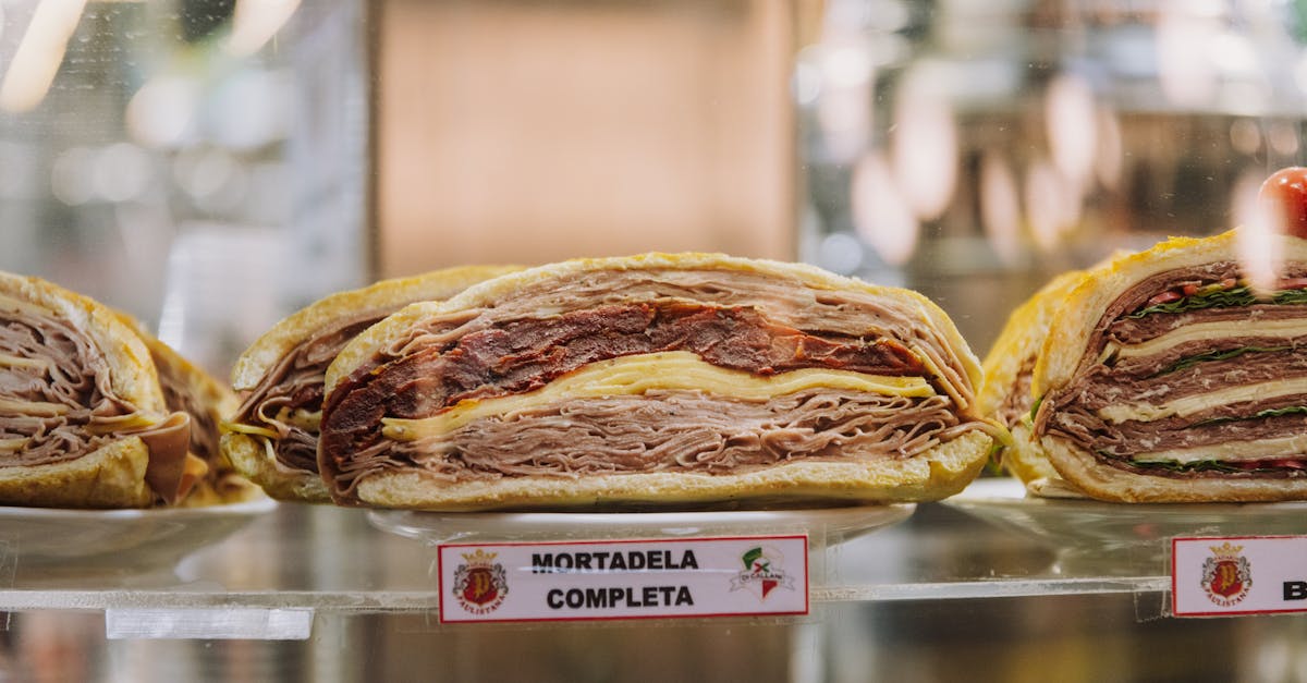 close up of assorted sandwiches with mortadela cheese and greens on display at a deli or bakery