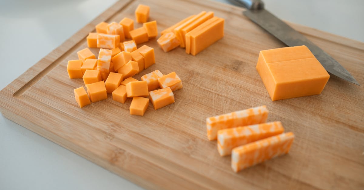 close up of cheddar and colby jack cheese slices on a wooden cutting board with a knife