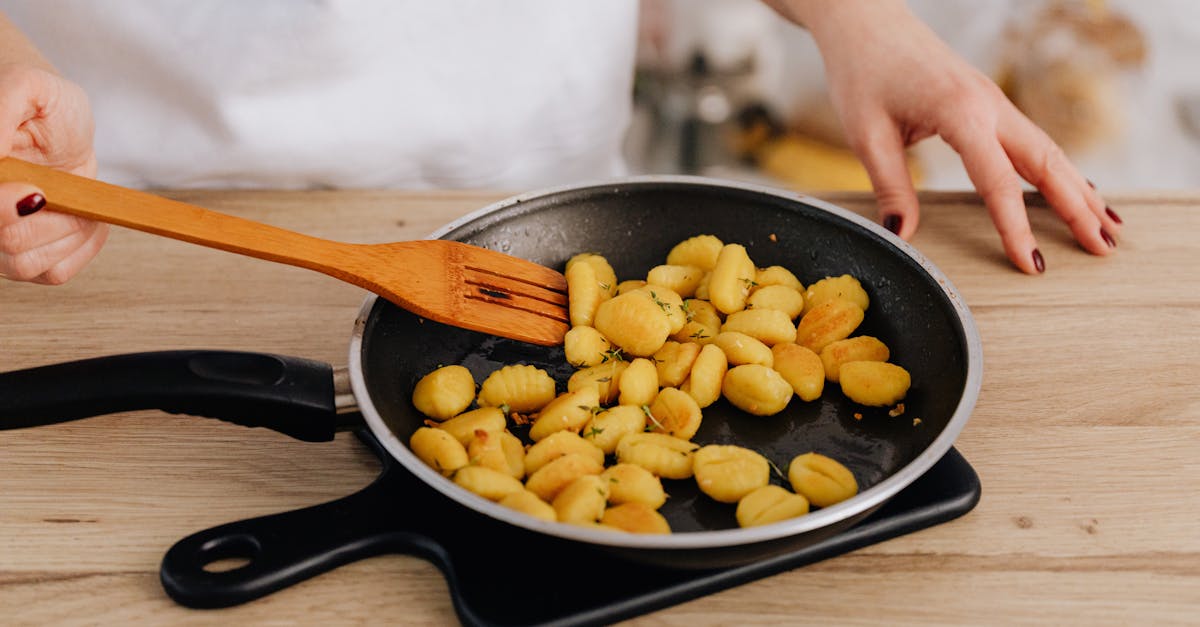 close up of cooking gnocchi in a pan using a wooden spatula on a wooden table