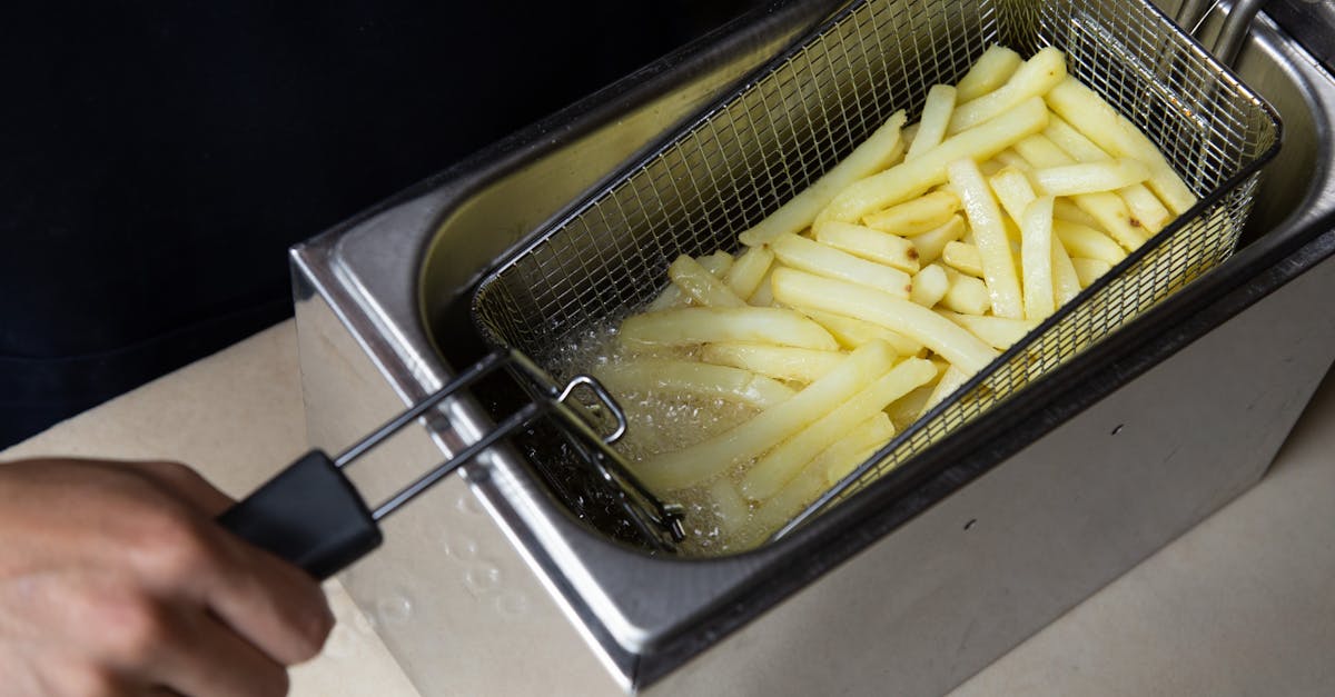 close up of french fries being deep fried in a commercial fryer hand holding the basket