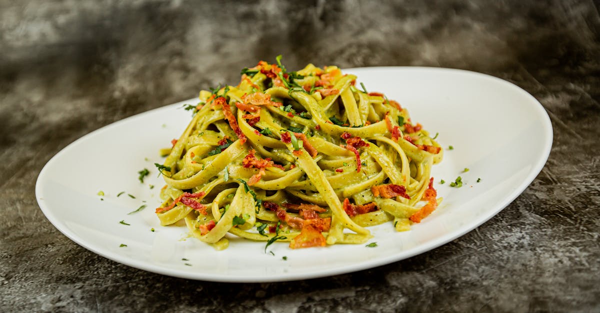 close up of freshly prepared pesto tagliatelle pasta with sun dried tomatoes on a white plate