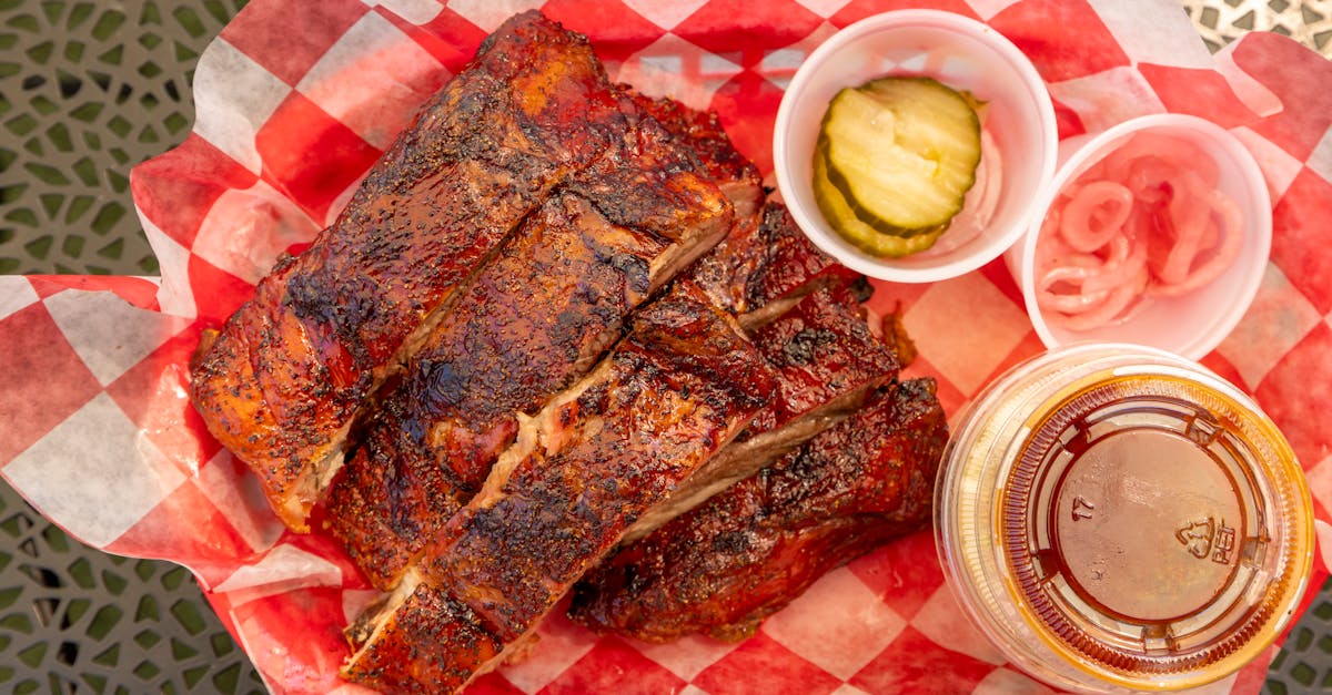 close up of grilled barbecue ribs with pickles onions and sauce on picnic table