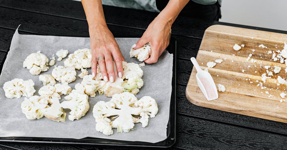 close up of hands arranging cauliflower on a baking tray for roasting showcasing food preparation 1