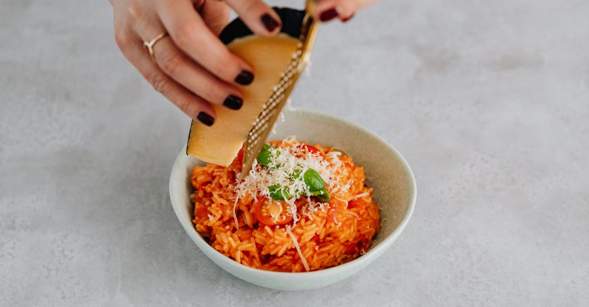 close up of hands grating parmesan cheese over a delicious bowl of tomato risotto