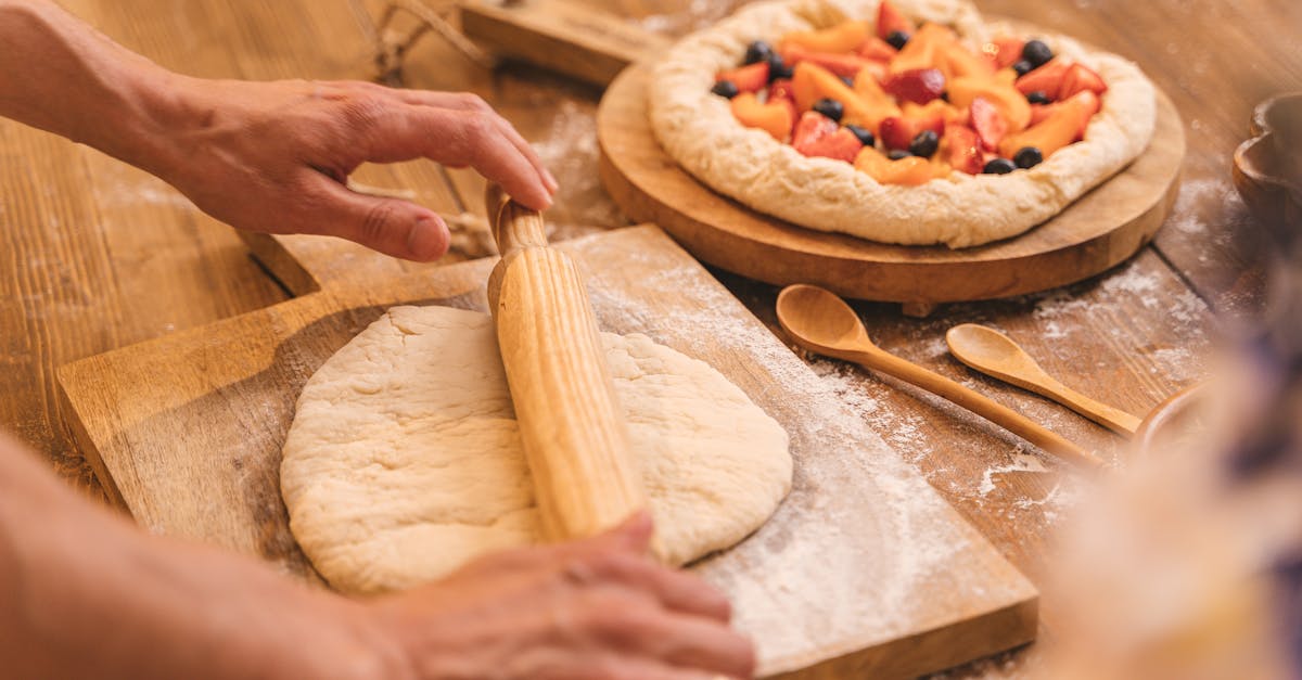 close up of hands rolling dough with a fruit pie nearby on a wooden table 1