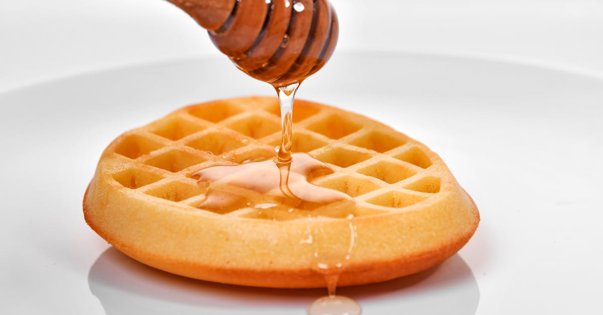close up of honey being drizzled from a dipper onto a golden waffle on a white plate 1