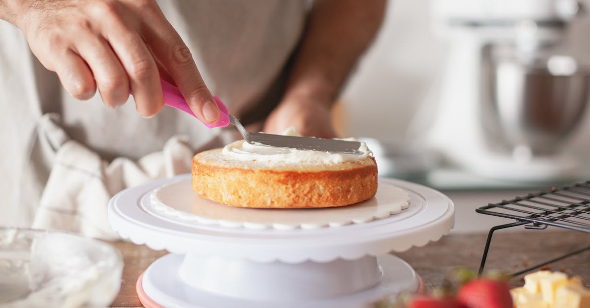 close up of person decorating a cake with frosting using a pink spatula on a cake stand 2