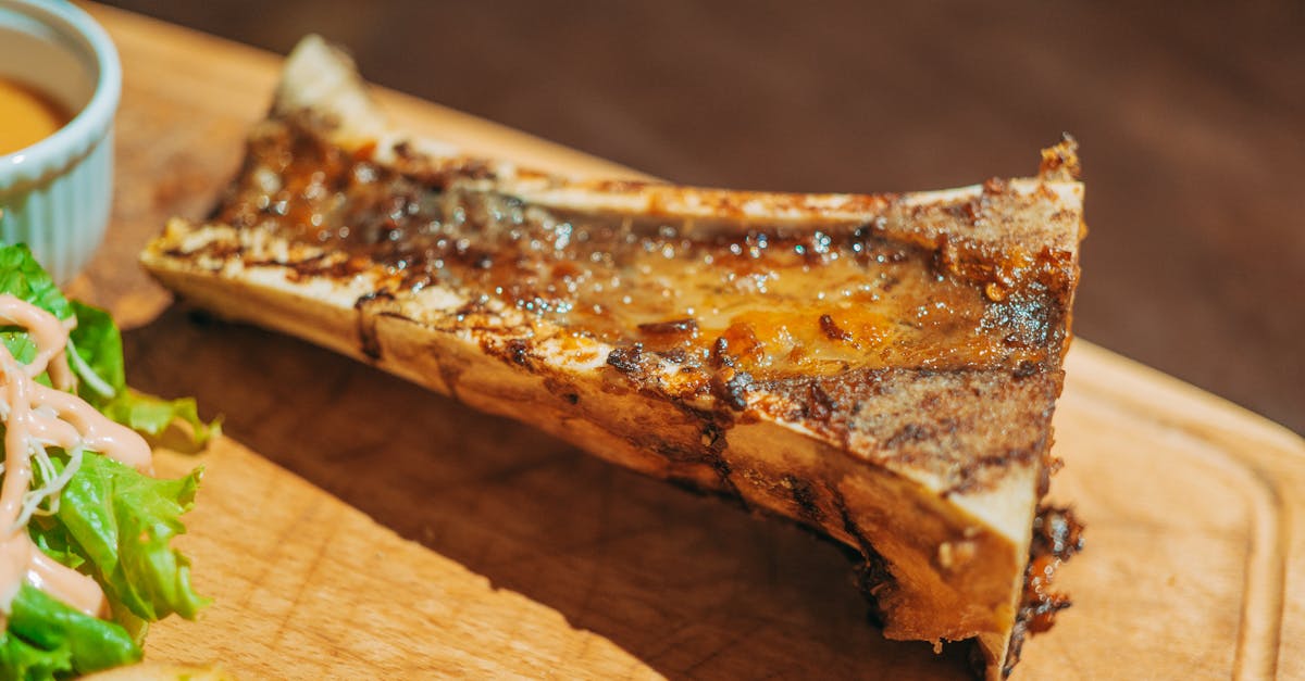 close up of roasted bone marrow served on a wooden board with salad and sauce 3