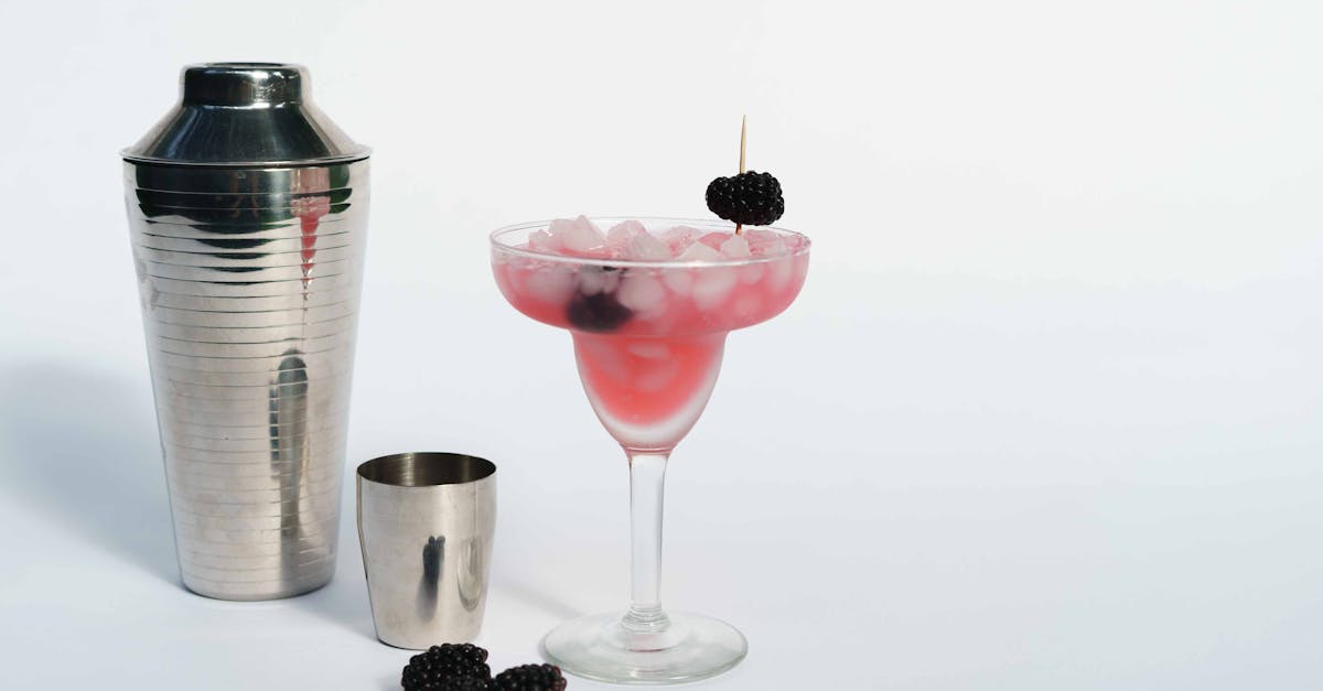 cold refreshing margarita cocktail made of ice cubes and blackberries placed near shaker on white ba 18
