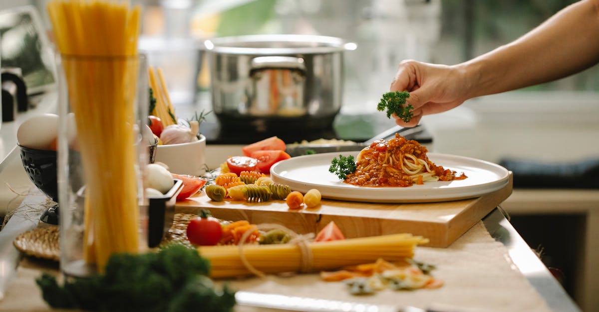 crop anonymous chef adding parsley to spaghetti with tomato and meat while cooking lunch in kitchen